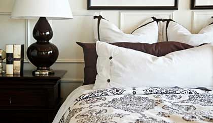A bedroom with a bed , nightstand , lamp and pillows. A bedroom with a bed , nightstand , lamp and pillows.