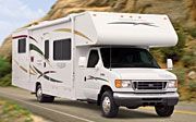 A white rv is driving down a road next to a mountain. A white rv is driving down a road next to a mountain.