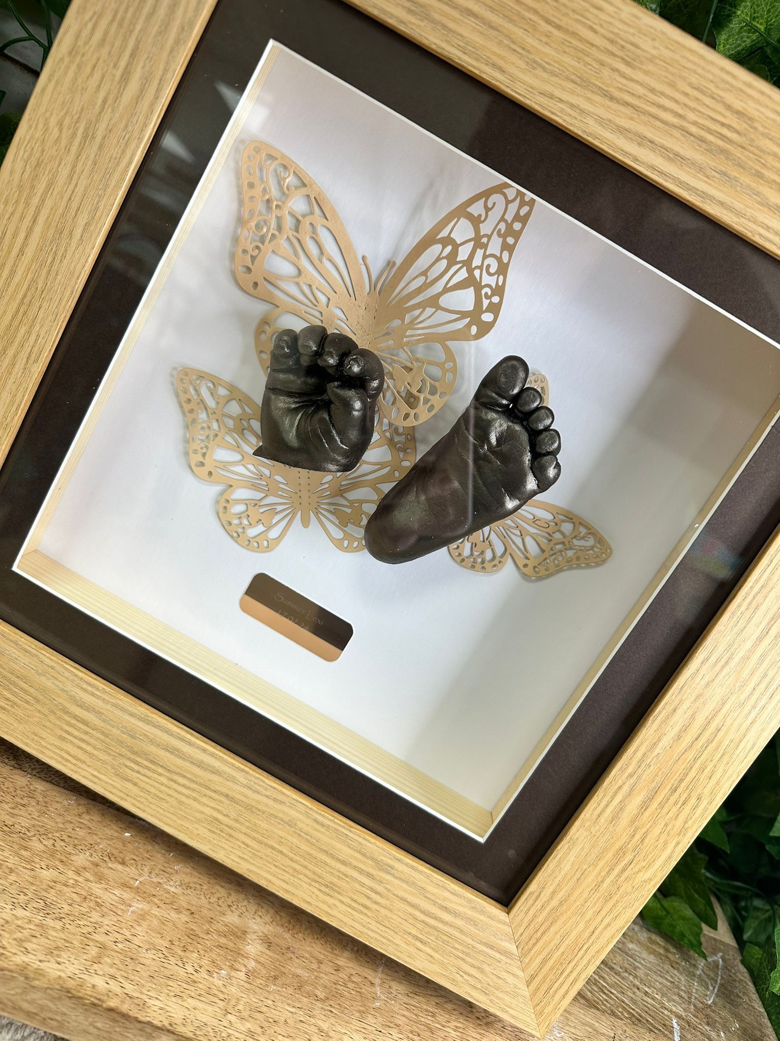 Shadow box frame with a baby's hand and foot casts, butterfly accents, and a wooden frame.