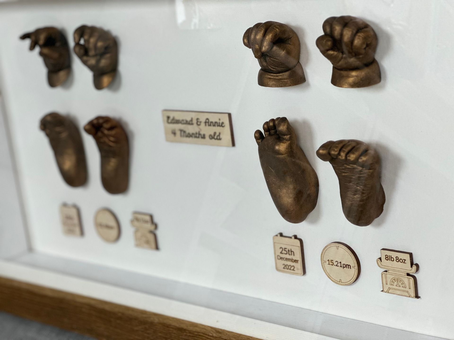 Bronze casts of baby hands and feet in a shadow box with personalized wooden labels.
