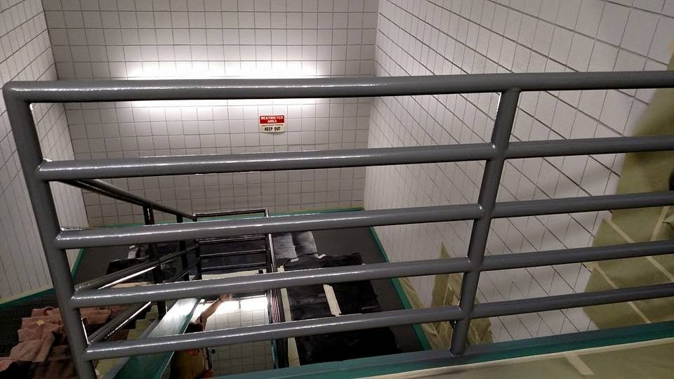 Stairwell with metal railing and tiled walls, looking down onto a medical stretcher.