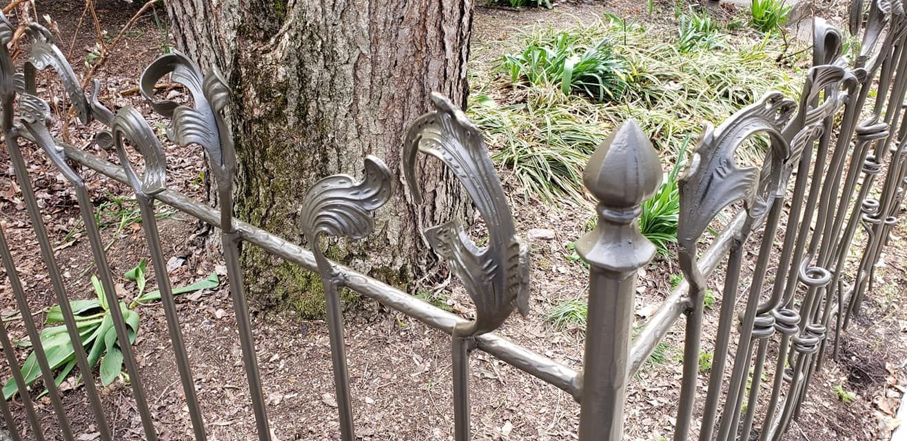 Ornate metal fence surrounding a tree trunk in a garden.
