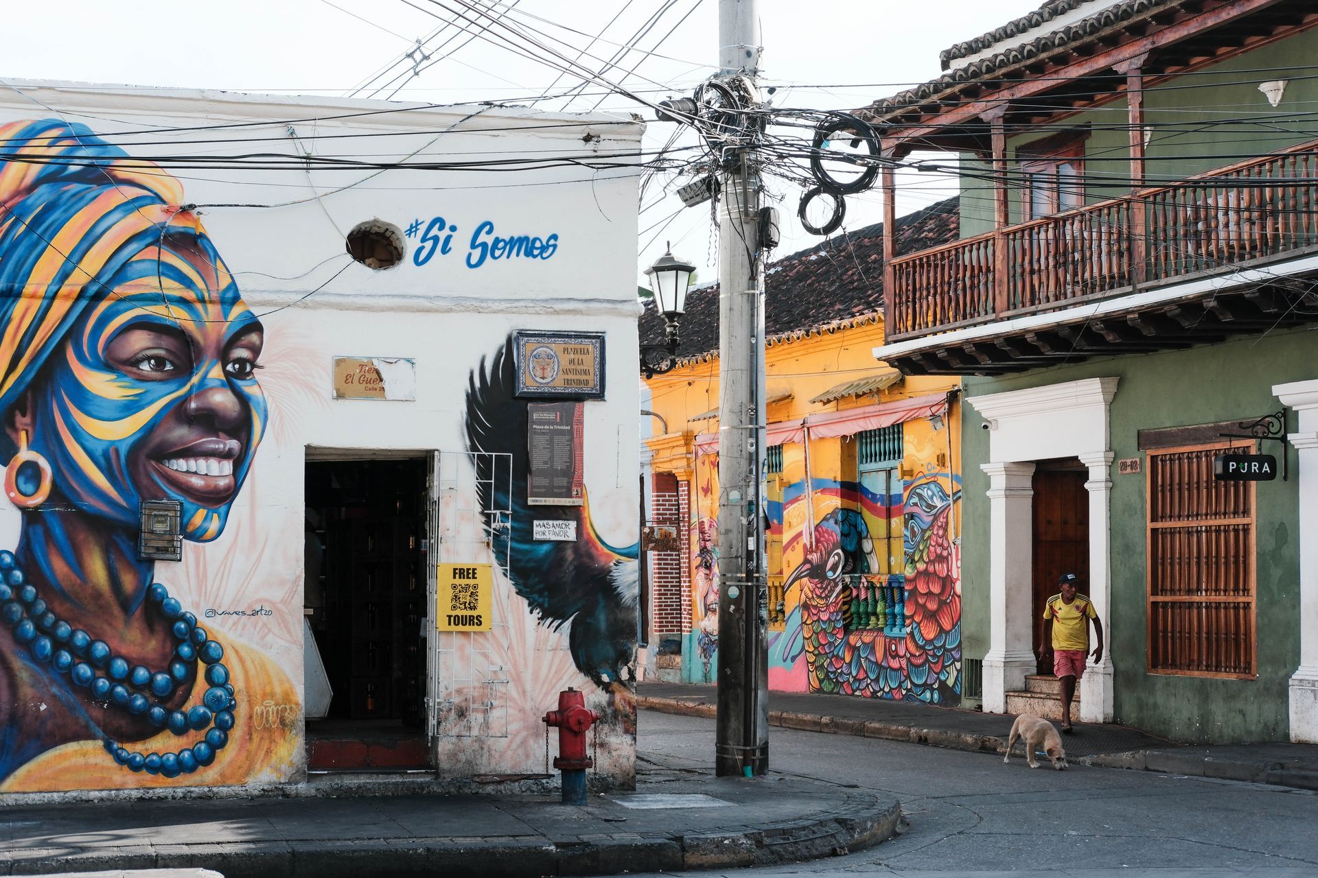 Un colorido callejón con sombrillas y banderas colgantes, que conduce a través de una calle sombreada bajo la luz del sol.