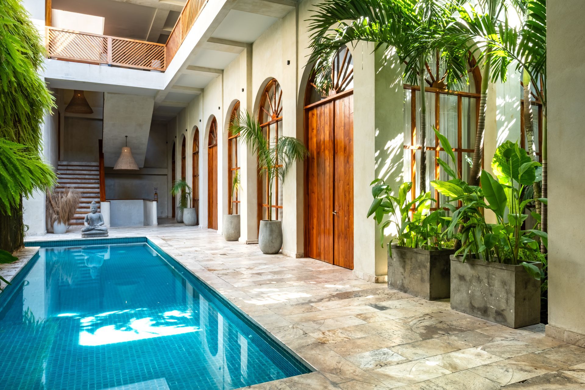 Patio moderno con piscina turquesa, patio de piedra, ventanas arqueadas y exuberantes plantas en macetas.