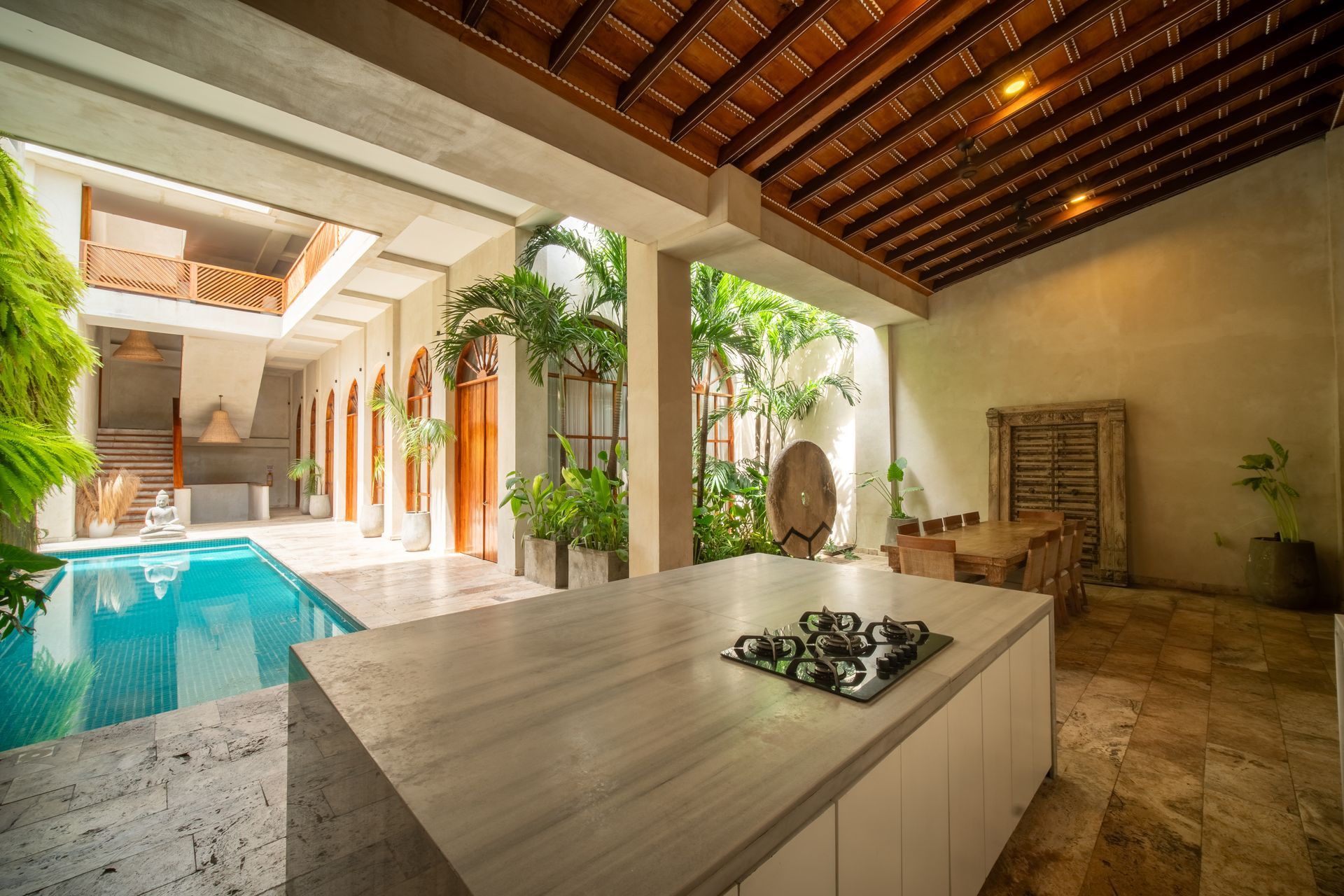 Patio de lujo con piscina, zona de estar y mesa de mármol bajo un techo de listones de madera.