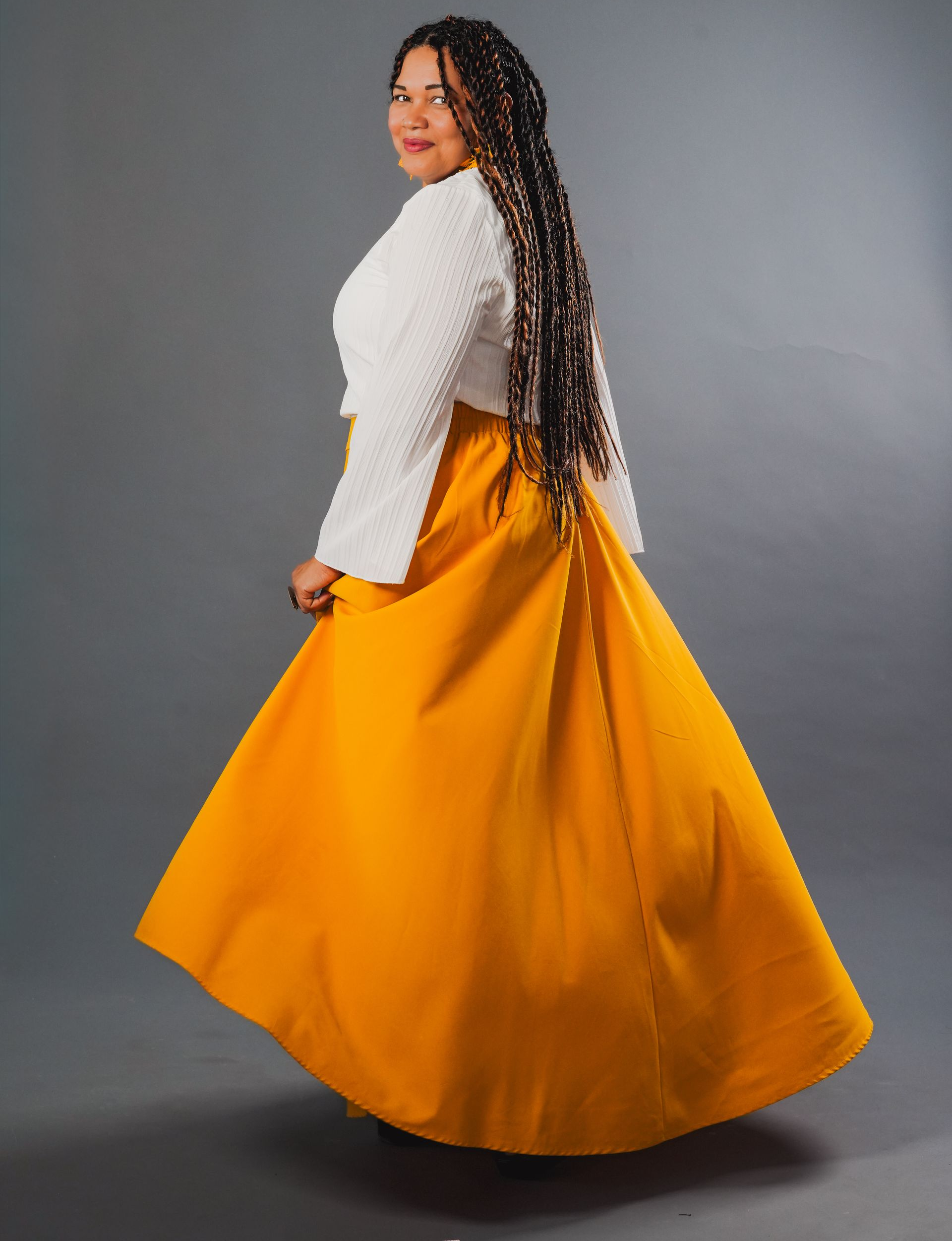 Una persona con una blusa blanca y una falda naranja vaporosa, girando frente a un fondo de estudio gris.
