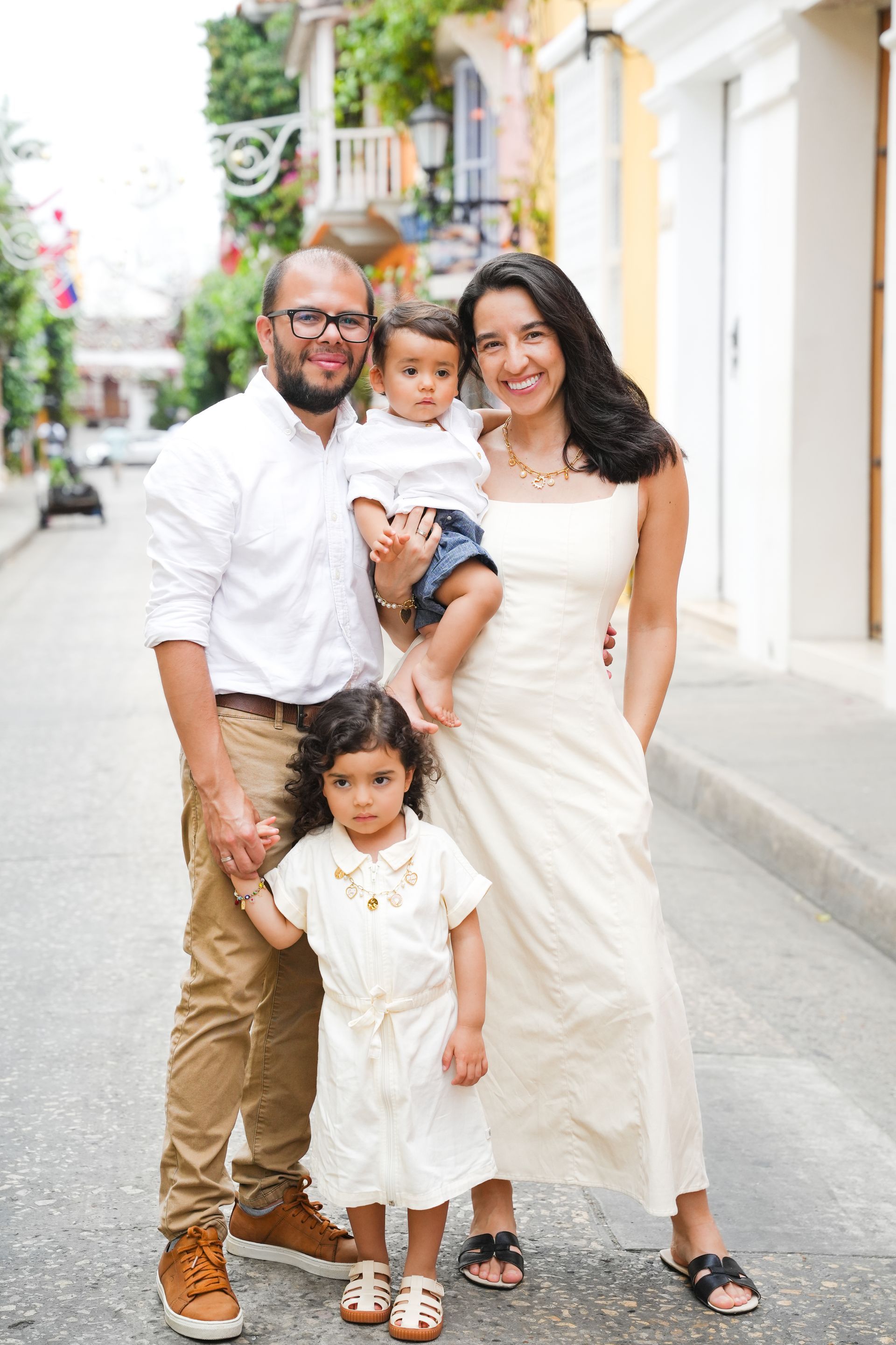 Familia de cuatro personas de pie en una calle soleada, vestida de blanco y beige, sonriendo a la cámara en cartagena