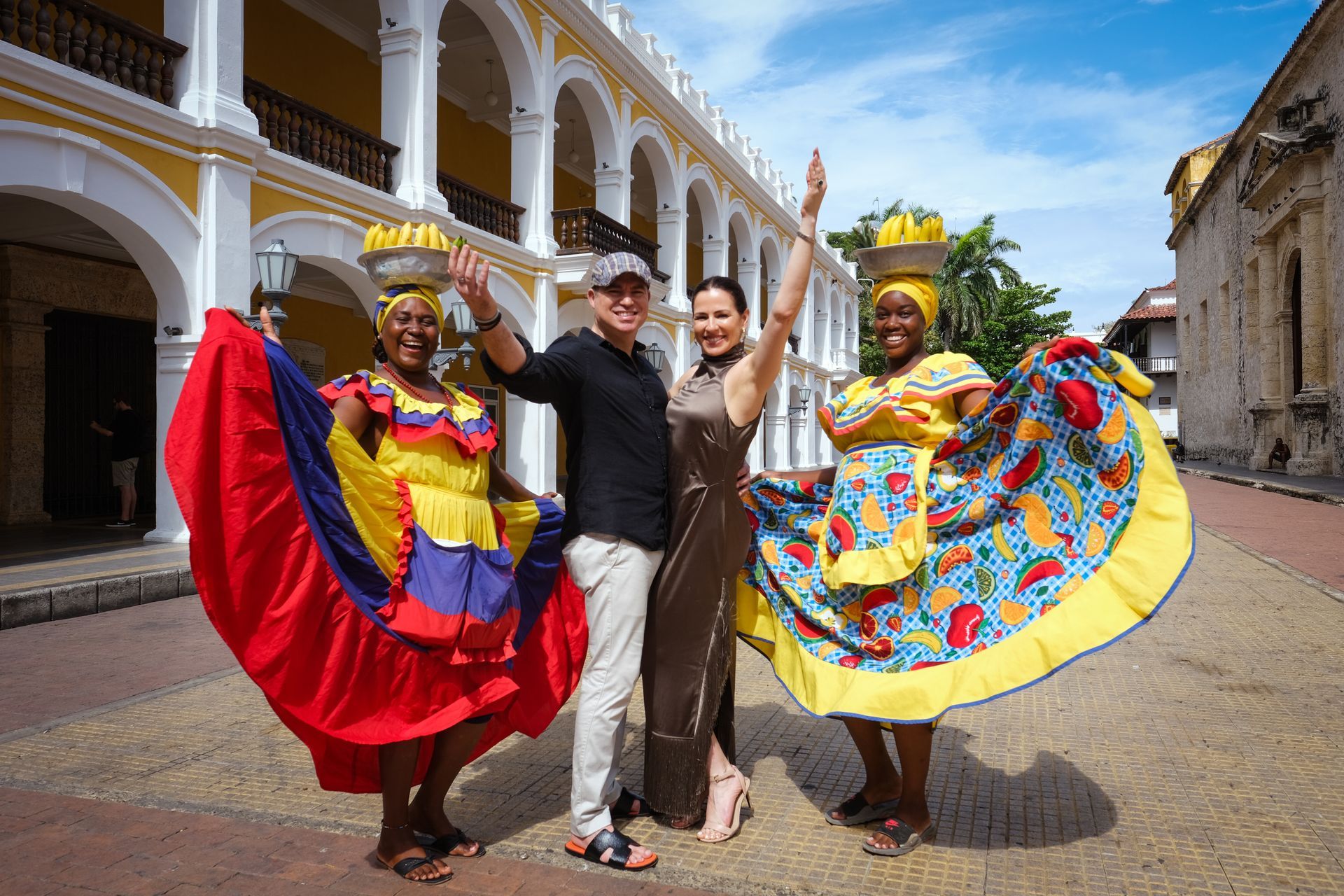 Cuatro personas bailando con coloridos trajes tradicionales en una calle empedrada junto a edificios coloniales.