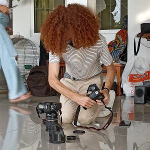 Un fotógrafo se agacha en el suelo con cámaras y equipo en una habitación interior luminosa.