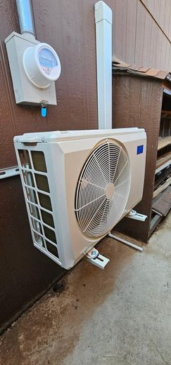 Outdoor wall-mounted air conditioner unit beside a white meter box on a brown exterior wall