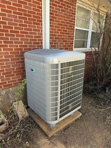 Outdoor central air conditioning unit beside a red brick house and window on a concrete pad.