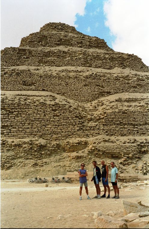 Vier mensen staan voor de trappenpiramide van Djoser in Egypte. Blauwe lucht met wolken.