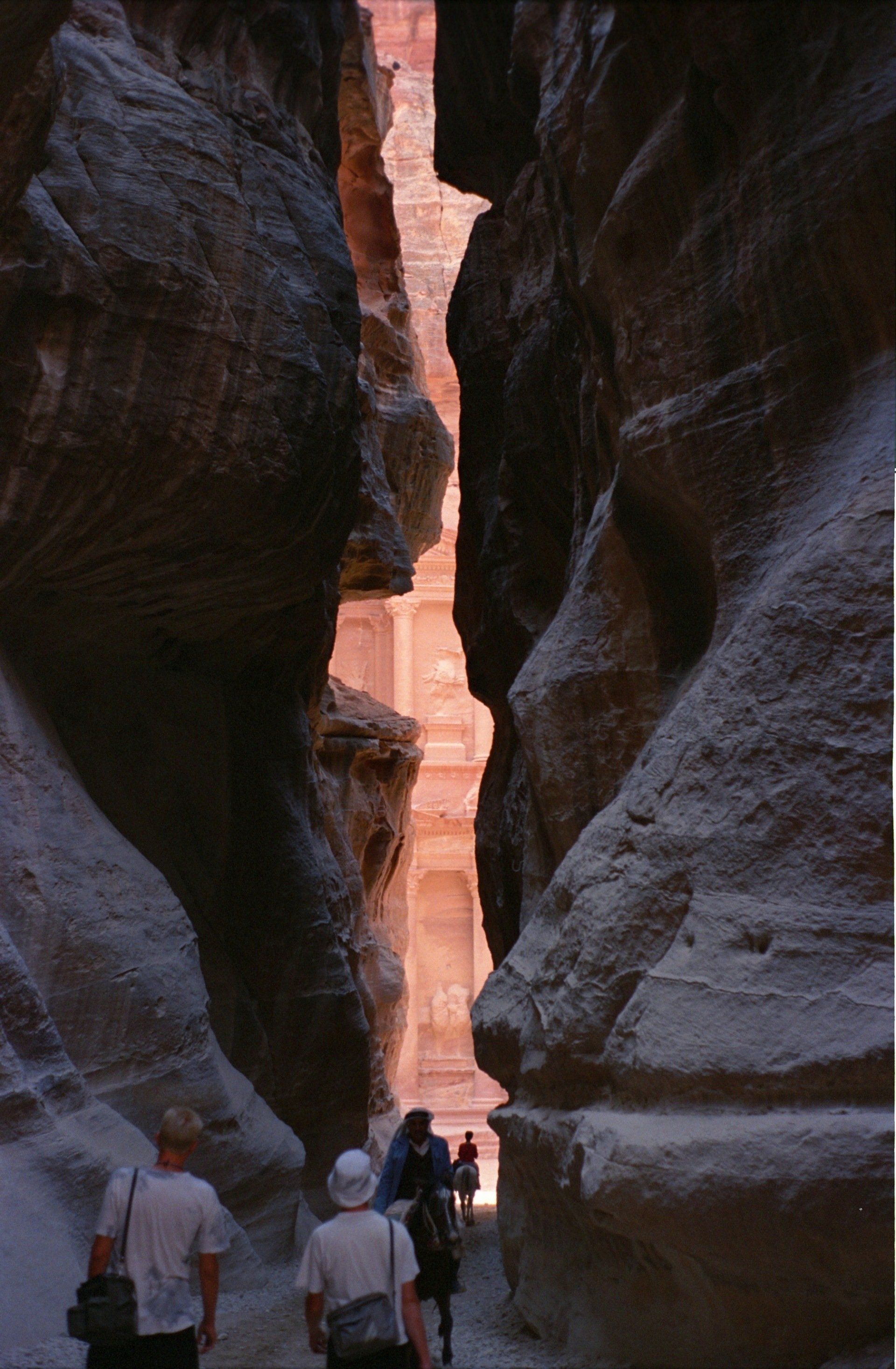 Smalle zandstenen kloof die leidt naar de Schatkamer van Petra in Jordanië. Toeristen lopen richting het licht.