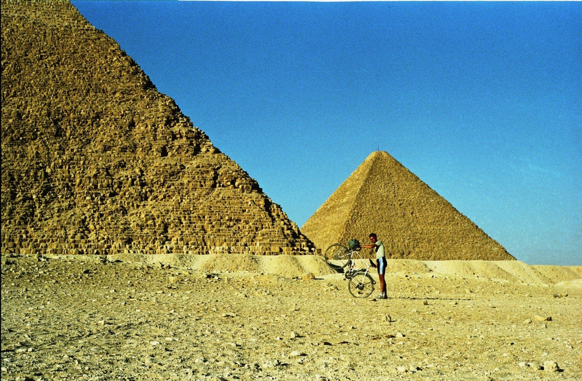 Twee piramides in de Egyptische woestijn met een persoon die ernaast staat met een fiets.