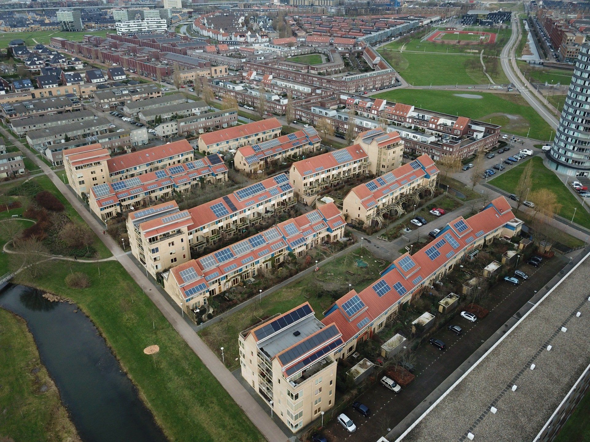 Luchtfoto van een woonwijk met rijen huizen, zonnepanelen op de daken en een moderne wolkenkrabber in de buurt.