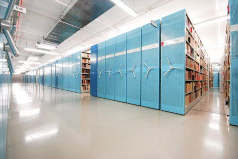 Rijen blauwe, verplaatsbare boekenkasten vol boeken in een helder verlicht archief.