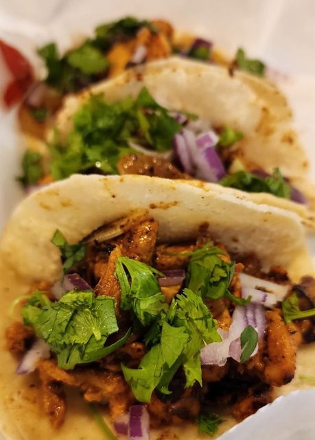 A close up of three tacos with meat , cilantro and onions on a table.