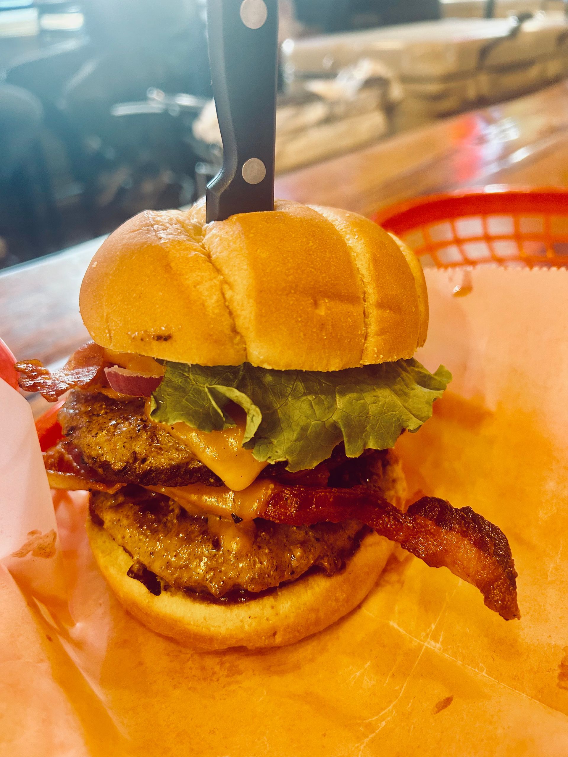 A close up of a hamburger with bacon and lettuce on a bun on a table.