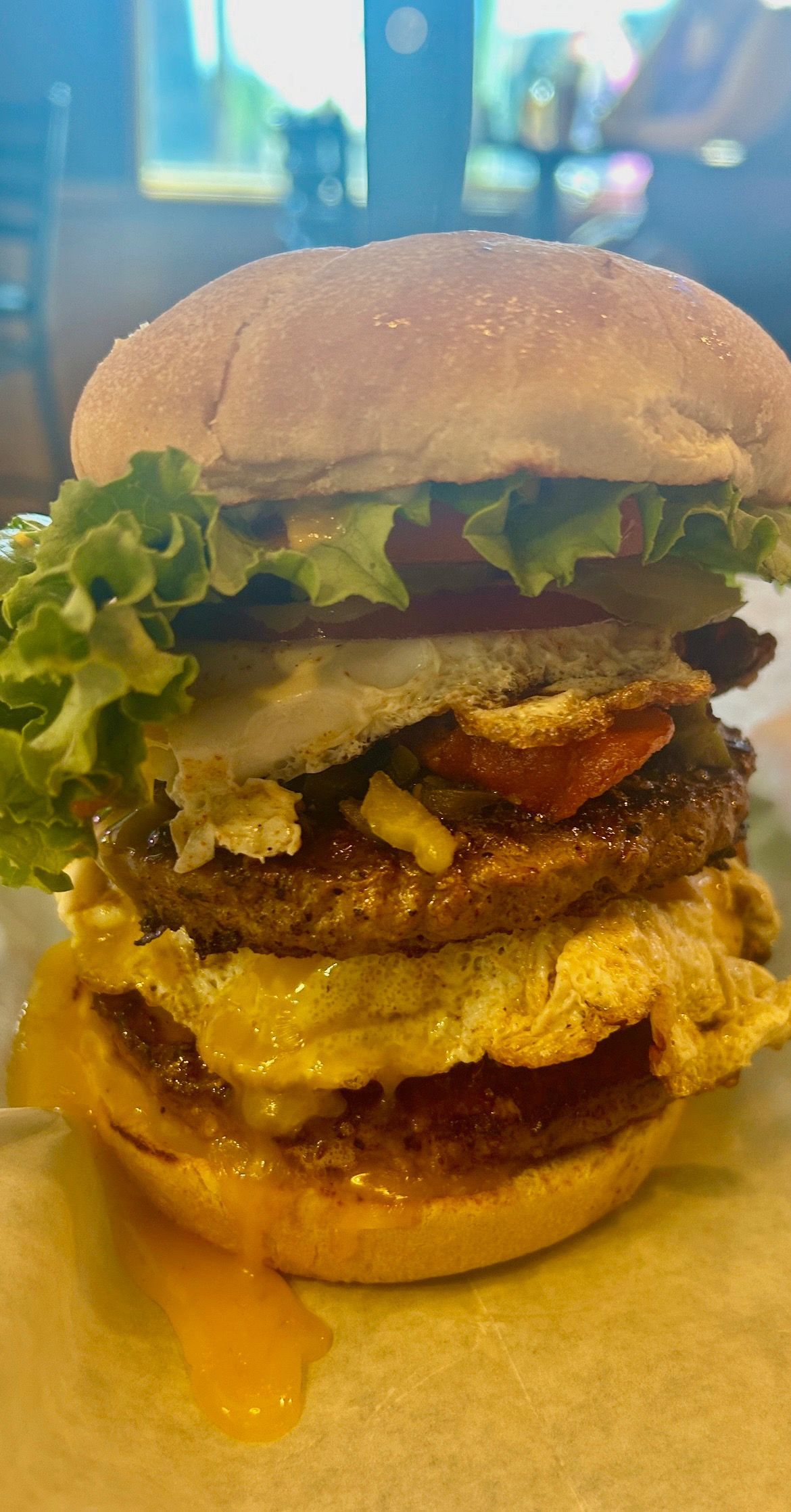 A close up of a hamburger with lettuce , tomatoes , cheese and eggs on a plate.