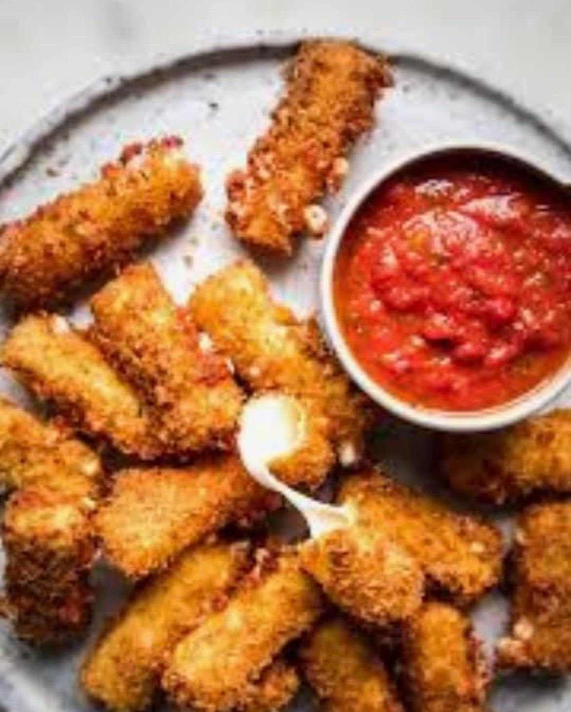A plate of fried mozzarella sticks with a bowl of tomato sauce.