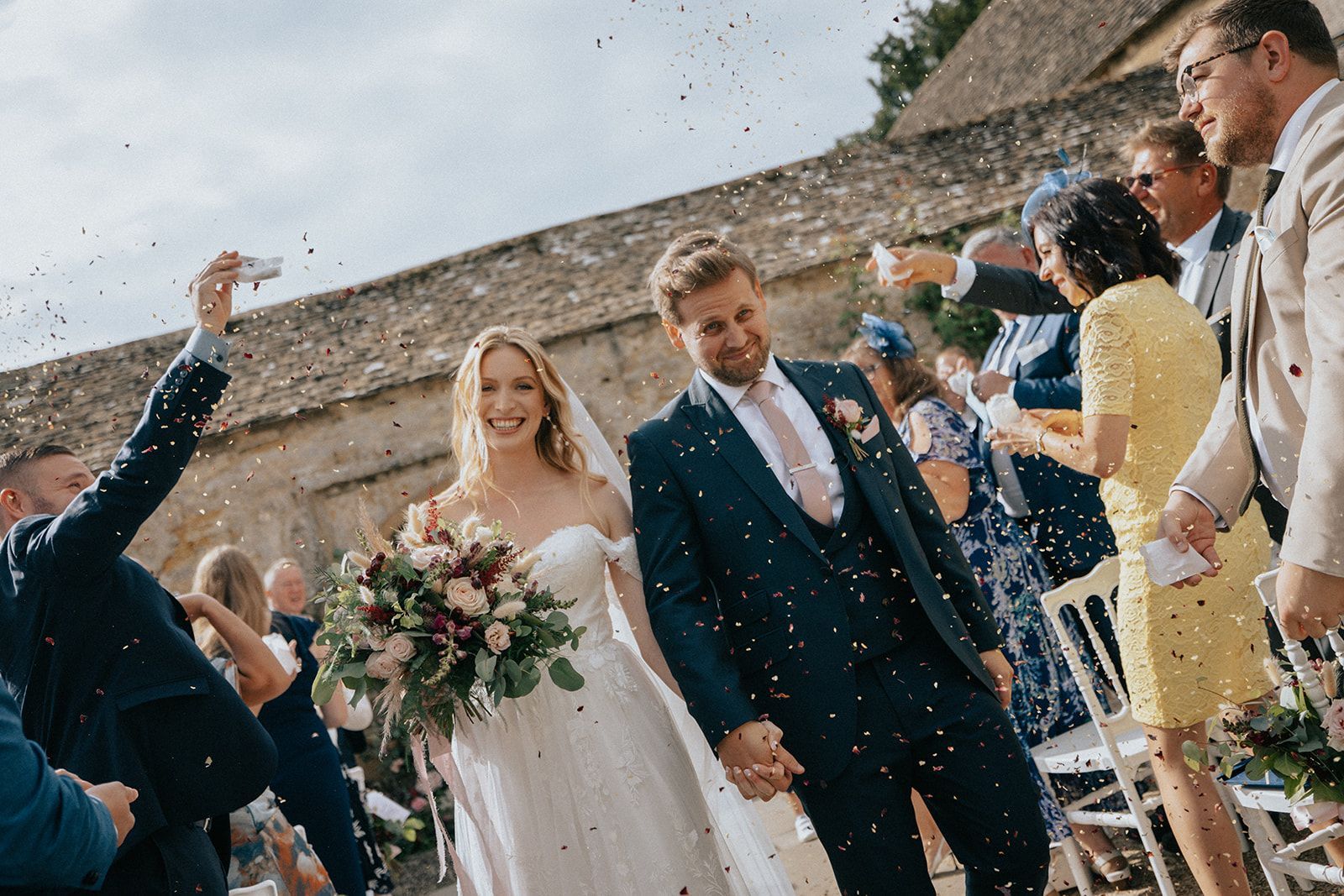 A bride and groom are walking down the aisle surrounded by confetti.