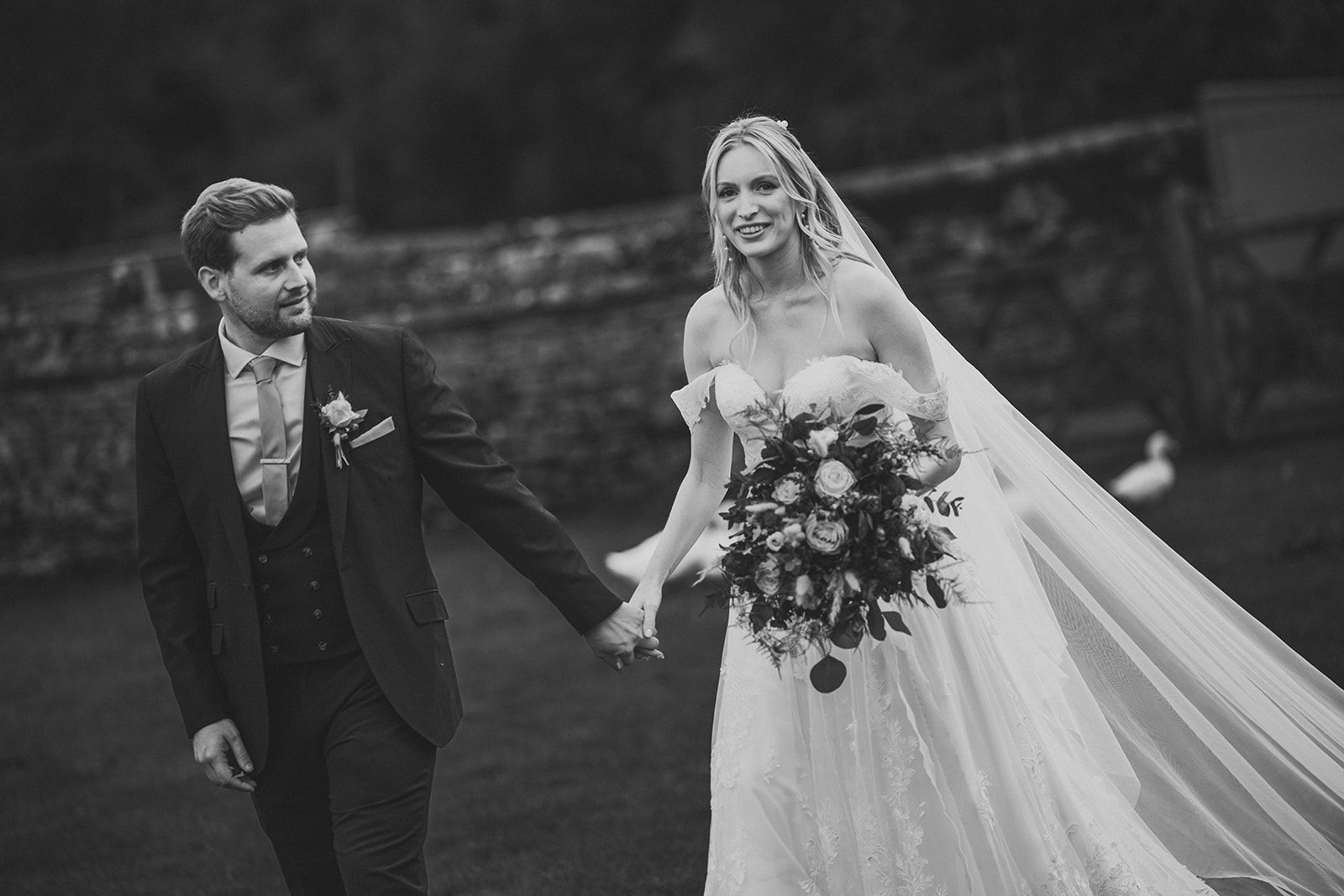 A black and white photo of a bride and groom holding hands.
