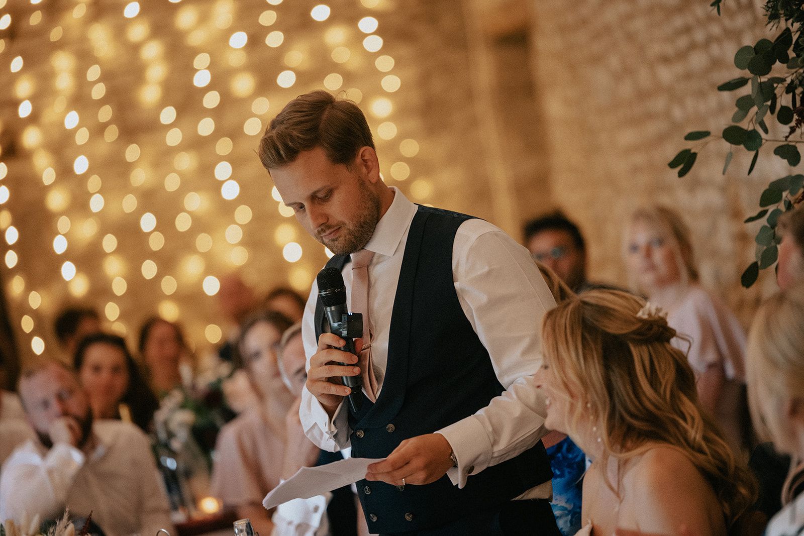 A man is giving a speech at a wedding reception while holding a microphone.