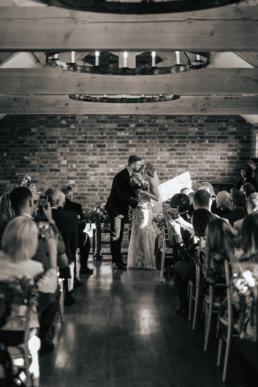 A black and white photo of a bride and groom kissing during their wedding ceremony.