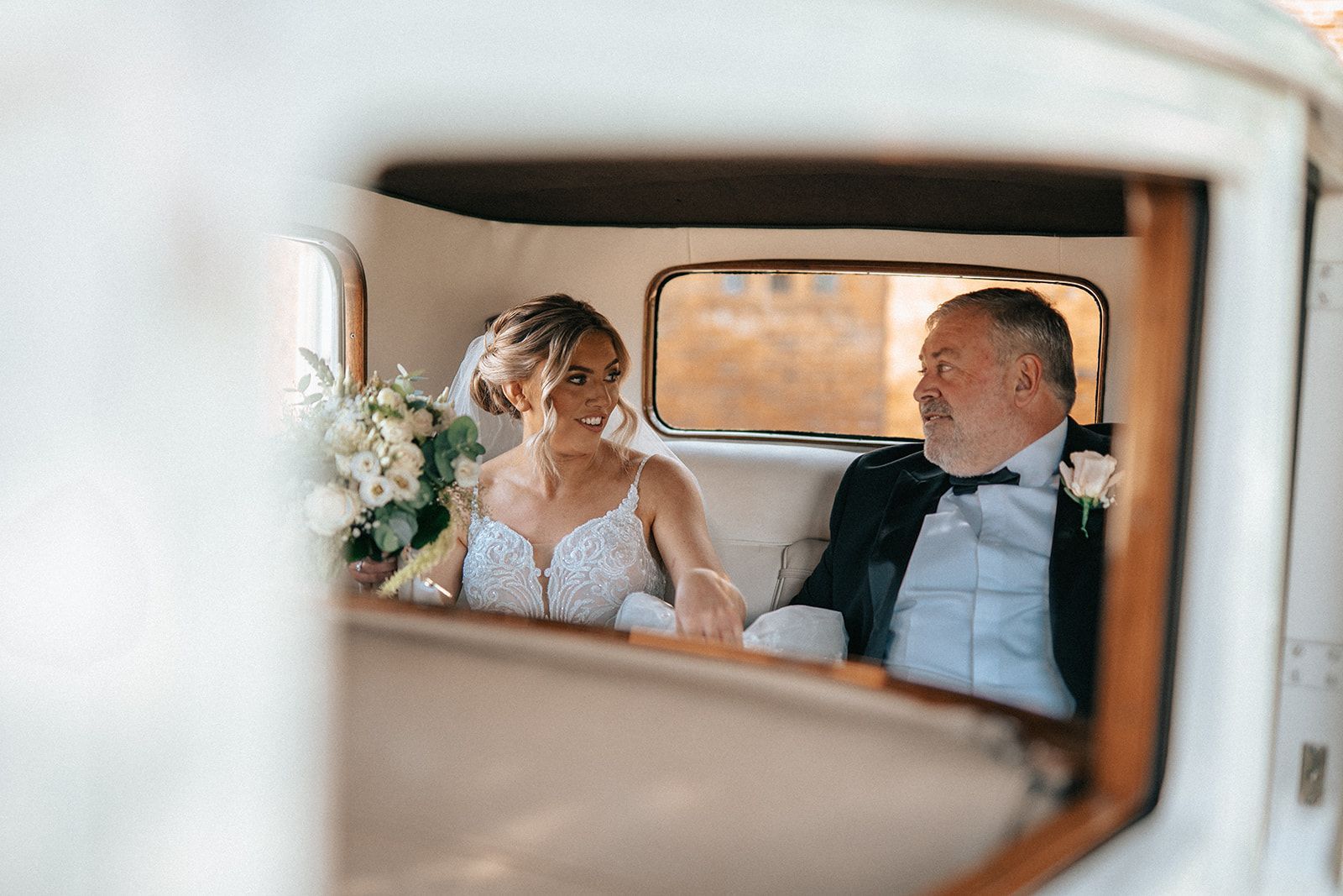 A bride and groom are sitting in the back seat of a car.