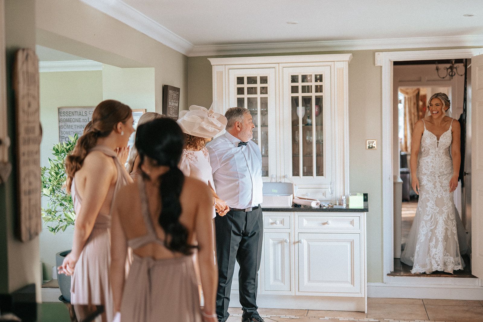 A bride and her bridesmaids are standing in a living room looking at their reflection in a mirror.