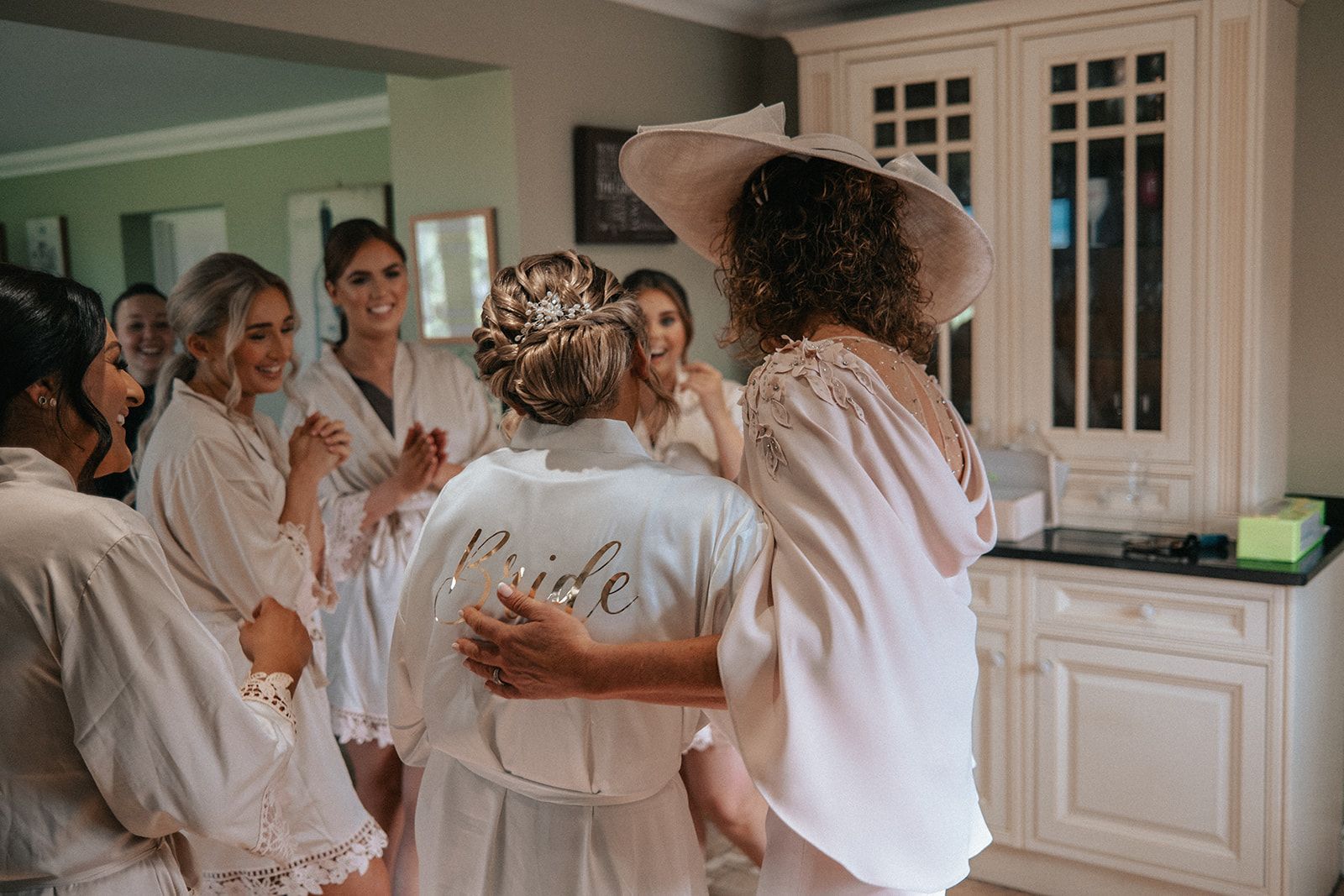 A bride and her bridesmaids are hugging each other in a room.