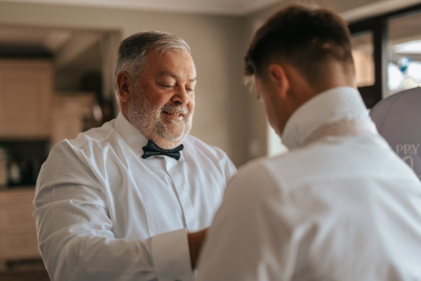 A man with a beard is helping another man with his bow tie.
