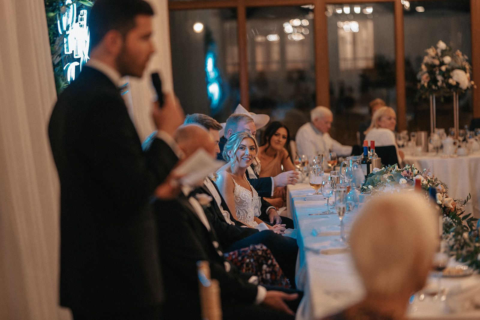 A man is giving a speech to a group of people at a wedding reception.