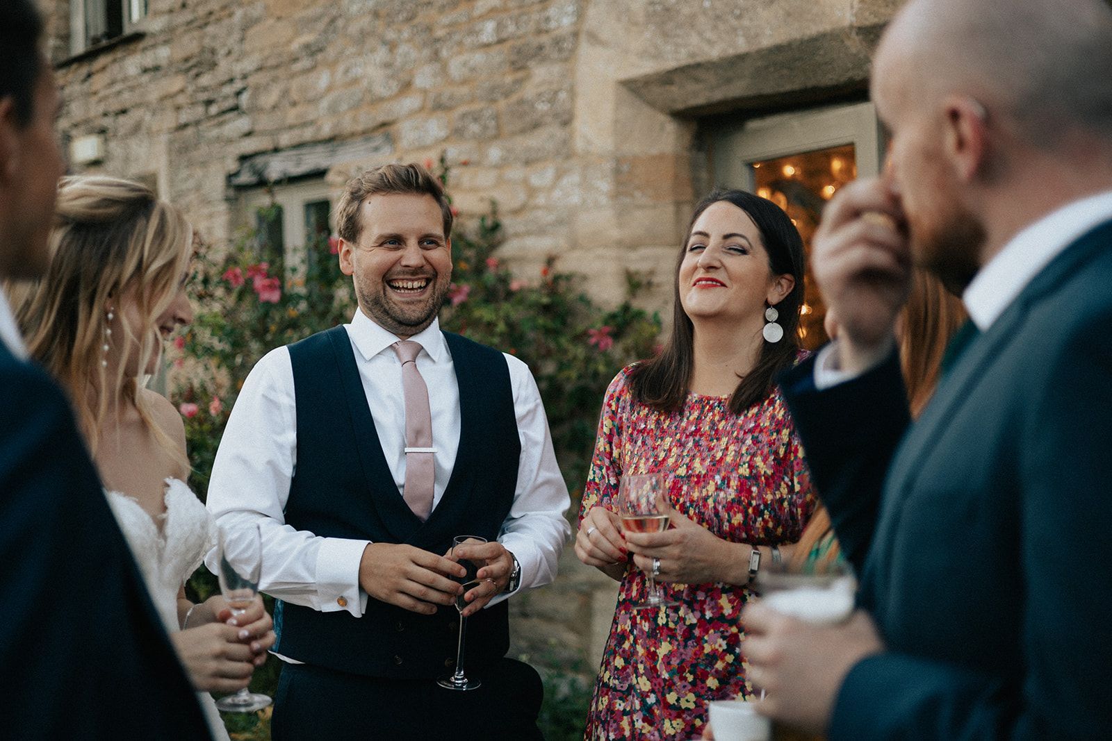 A group of people are standing around a man in a suit holding a glass of wine.