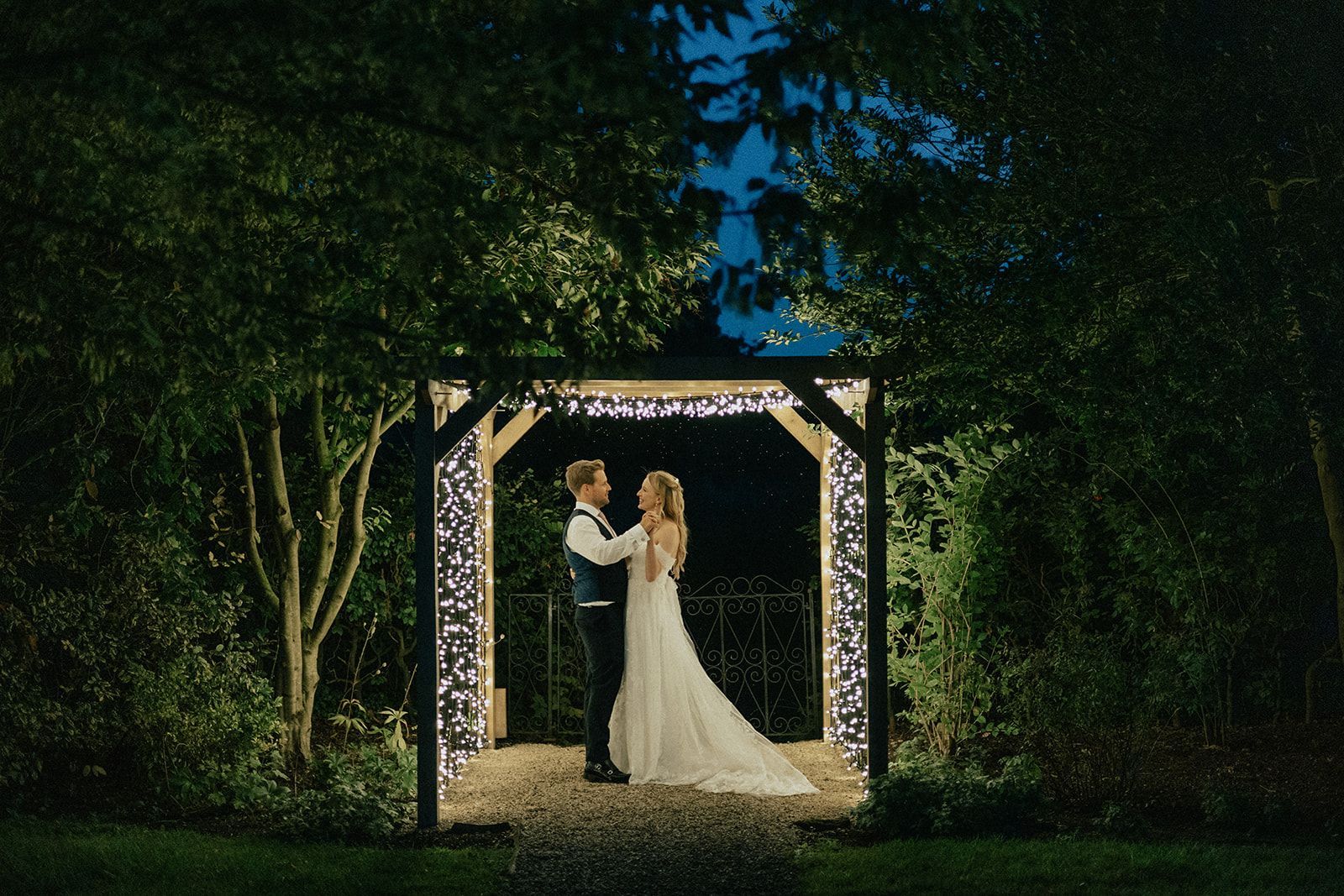 A bride and groom are dancing under a gazebo at night.