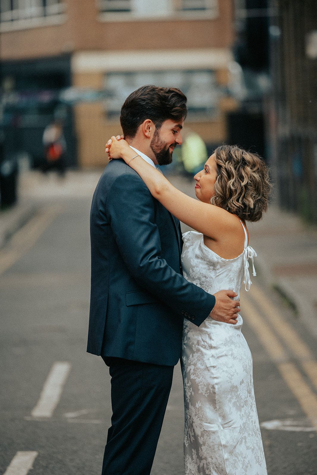 A bride and groom are standing next to each other on a city street.