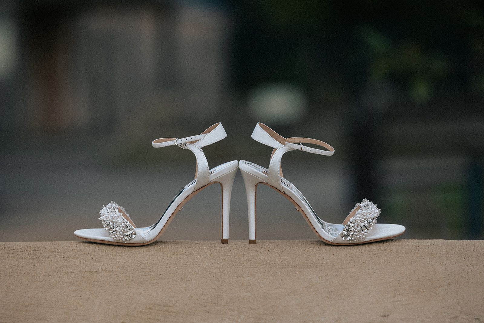 A pair of white wedding shoes are sitting on a wall.