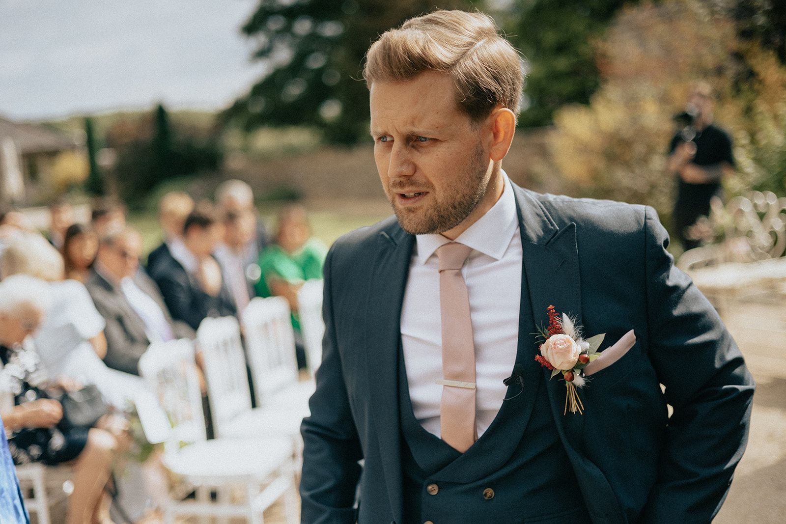 A man in a suit and tie is standing in front of a crowd of people at a wedding.