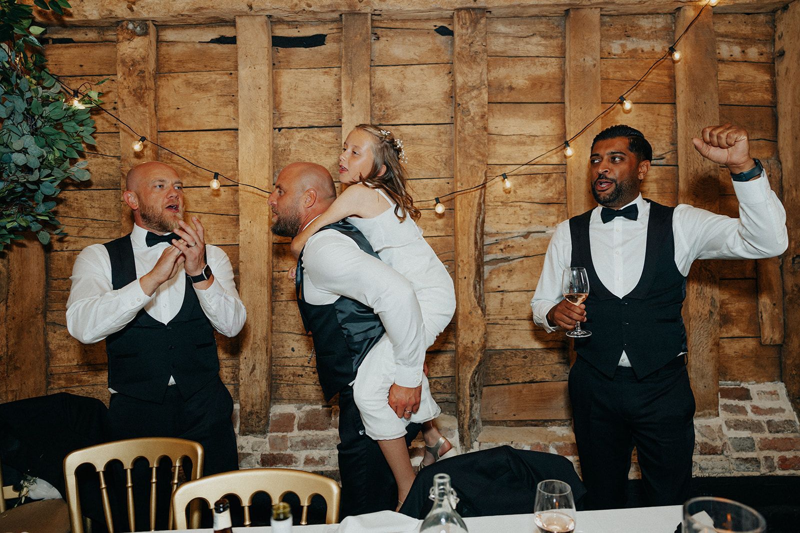 A man is carrying a little girl on his shoulders at a wedding reception.