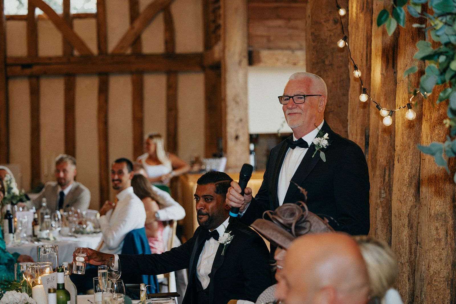 A man in a tuxedo is giving a speech at a wedding reception.