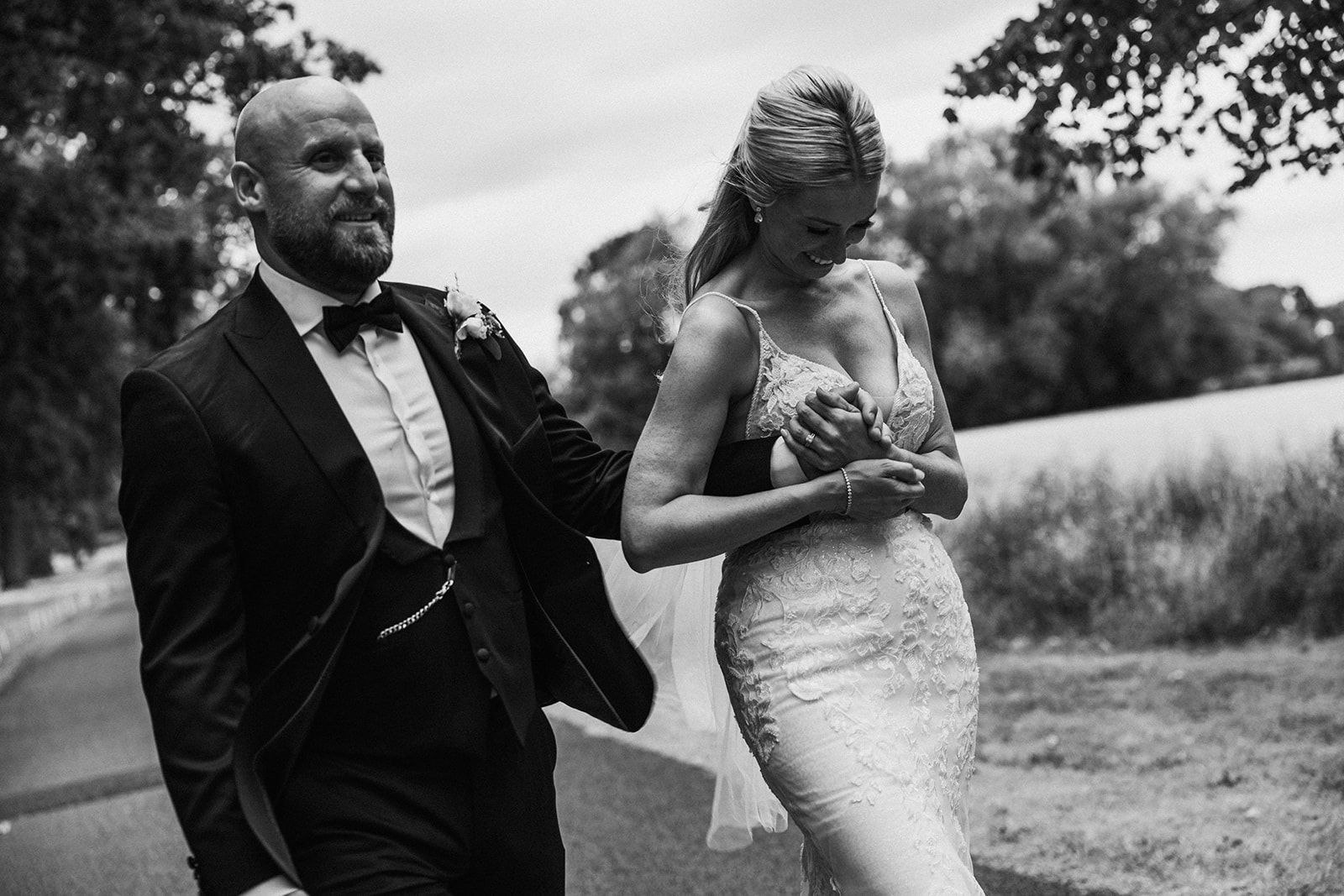 A black and white photo of a bride and groom walking down a road.