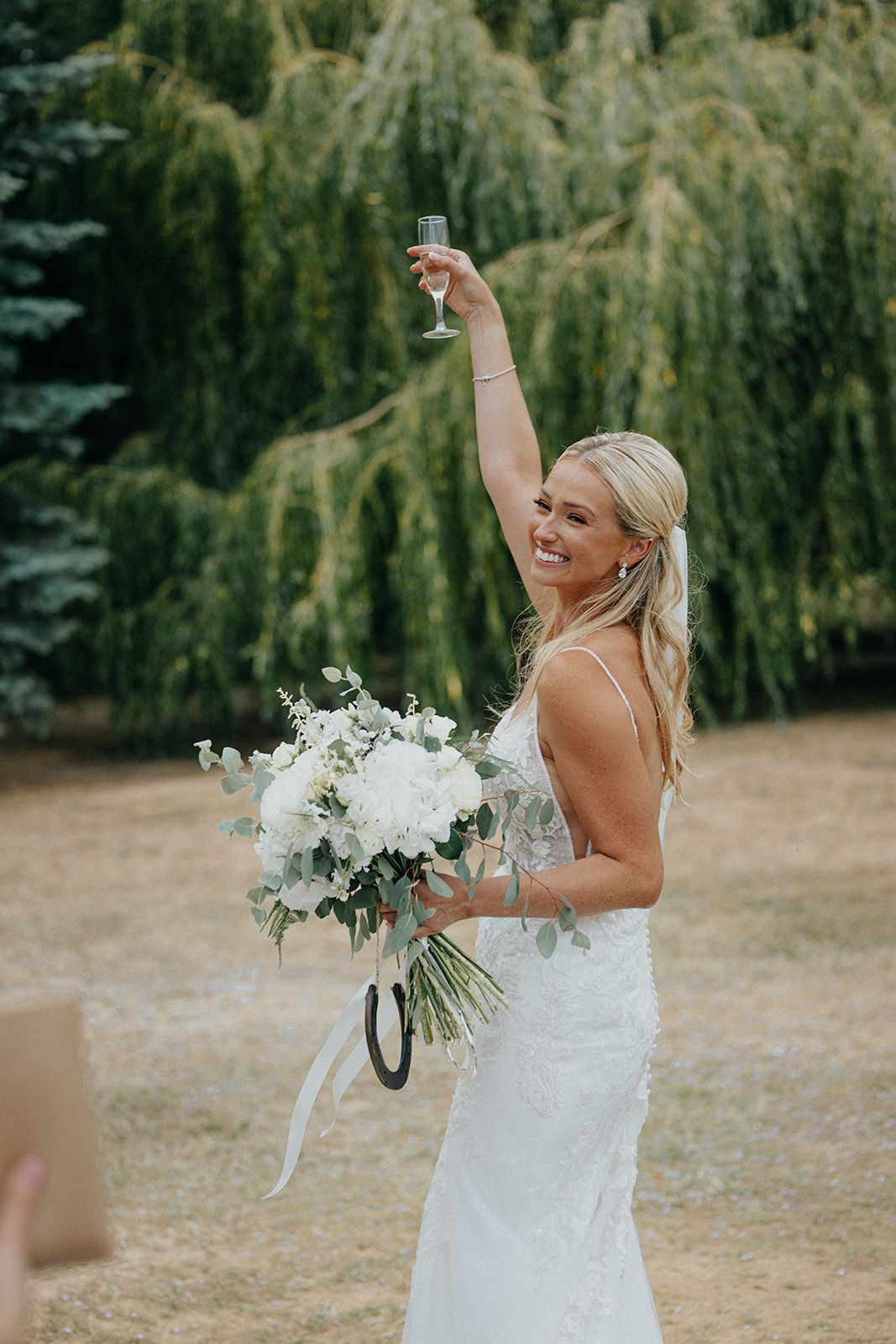 A bride in a white dress is holding a bouquet of flowers and a glass of champagne.