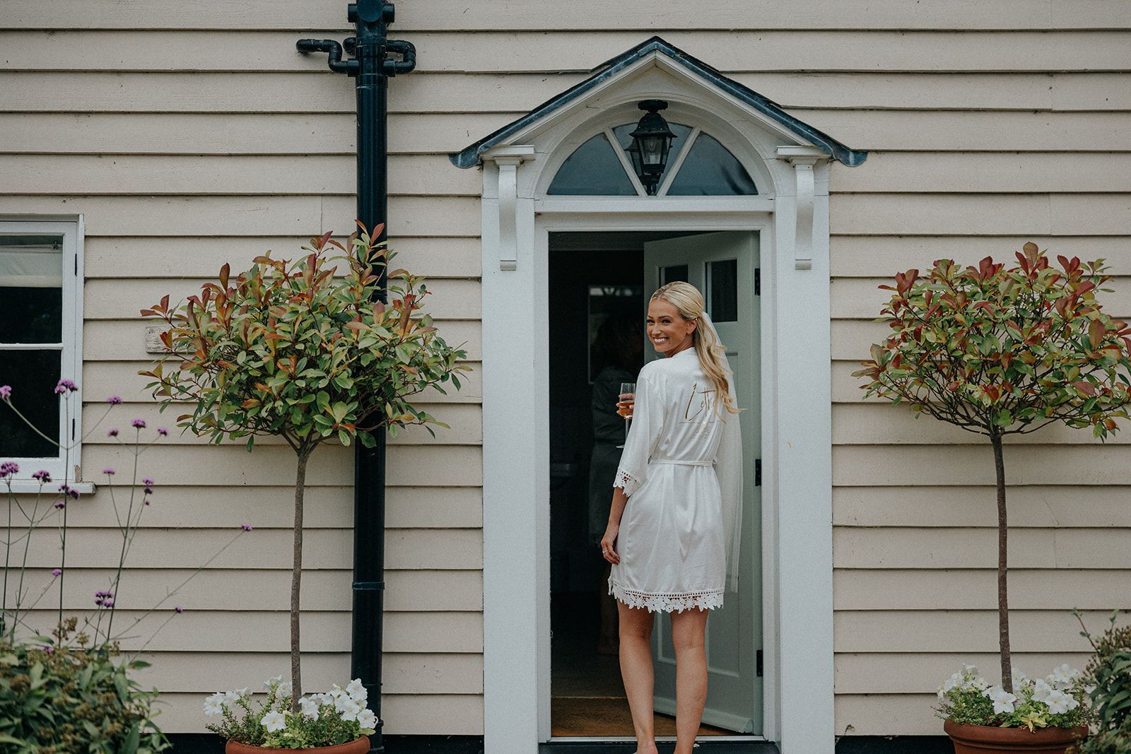 A woman in a white robe is standing in the doorway of a house.