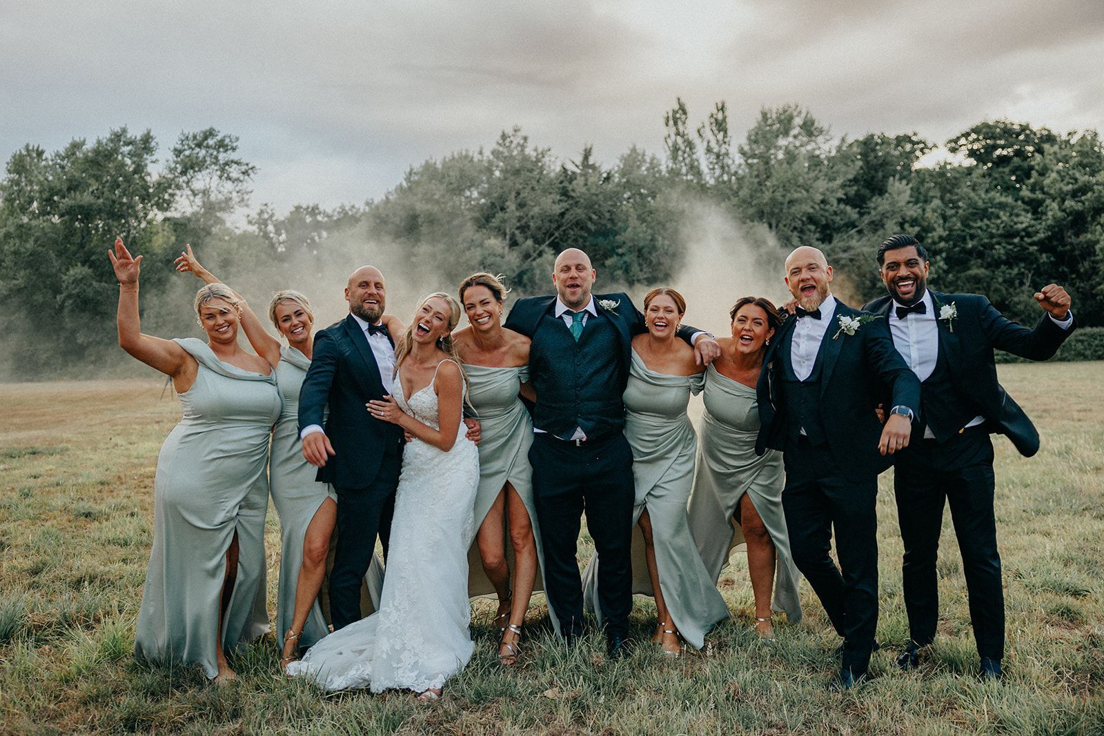 A bride and groom are posing for a picture with their wedding party in a field.