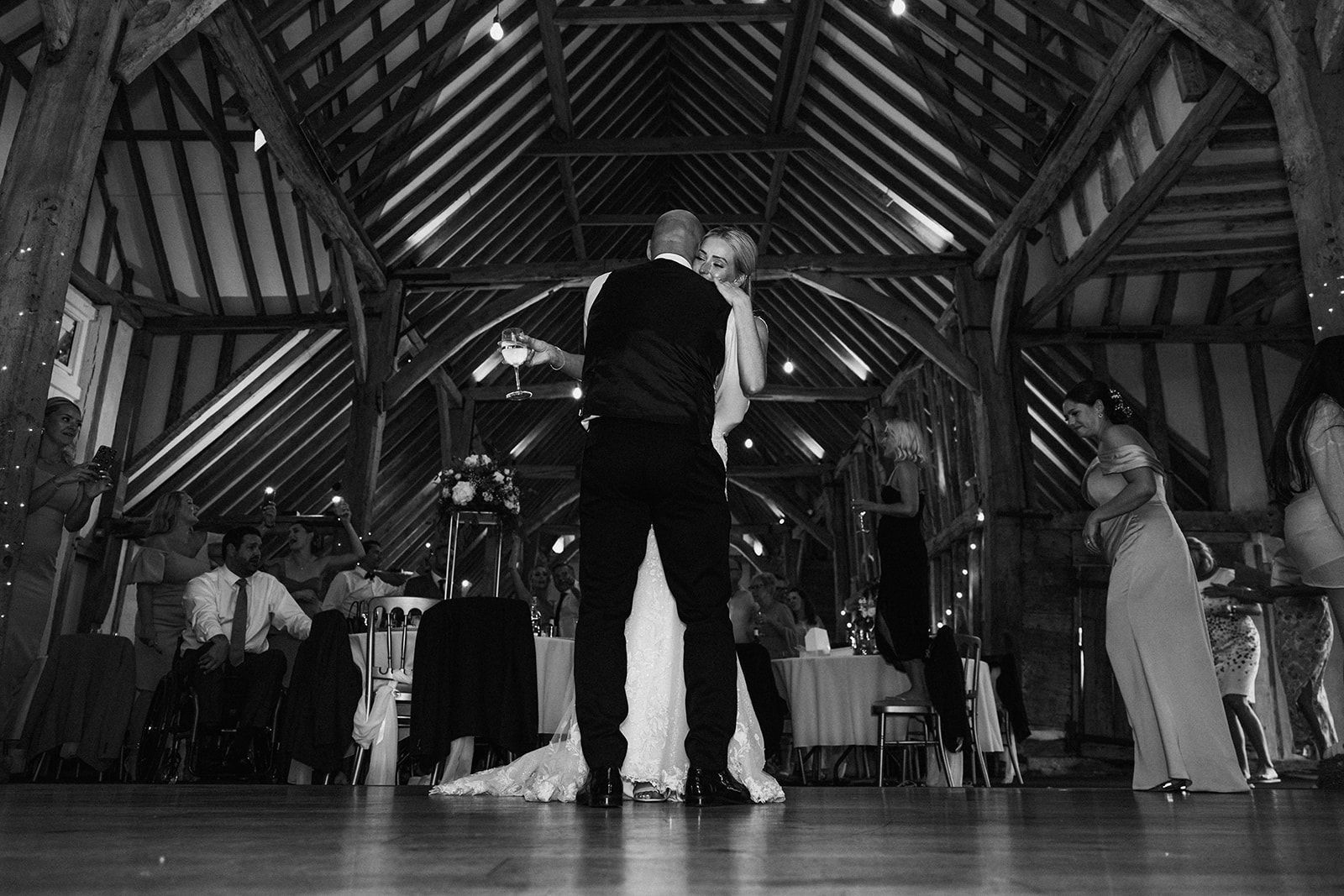 A black and white photo of a bride and groom dancing in a barn.