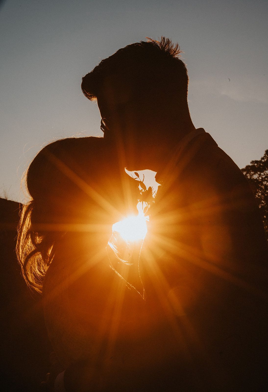 A man and a woman are kissing in front of the sun at sunset.