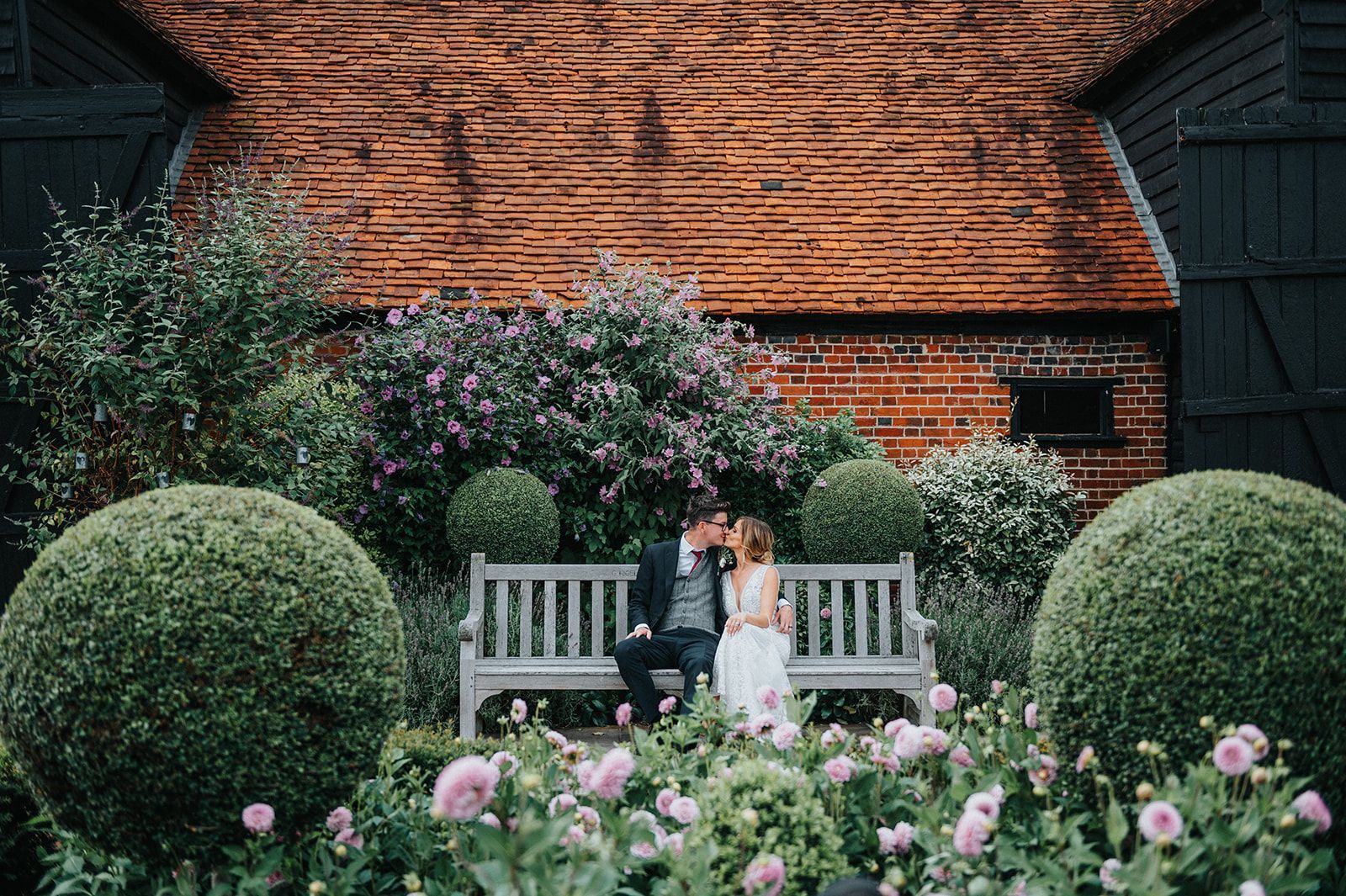 A bride and groom are sitting on a bench in a garden.