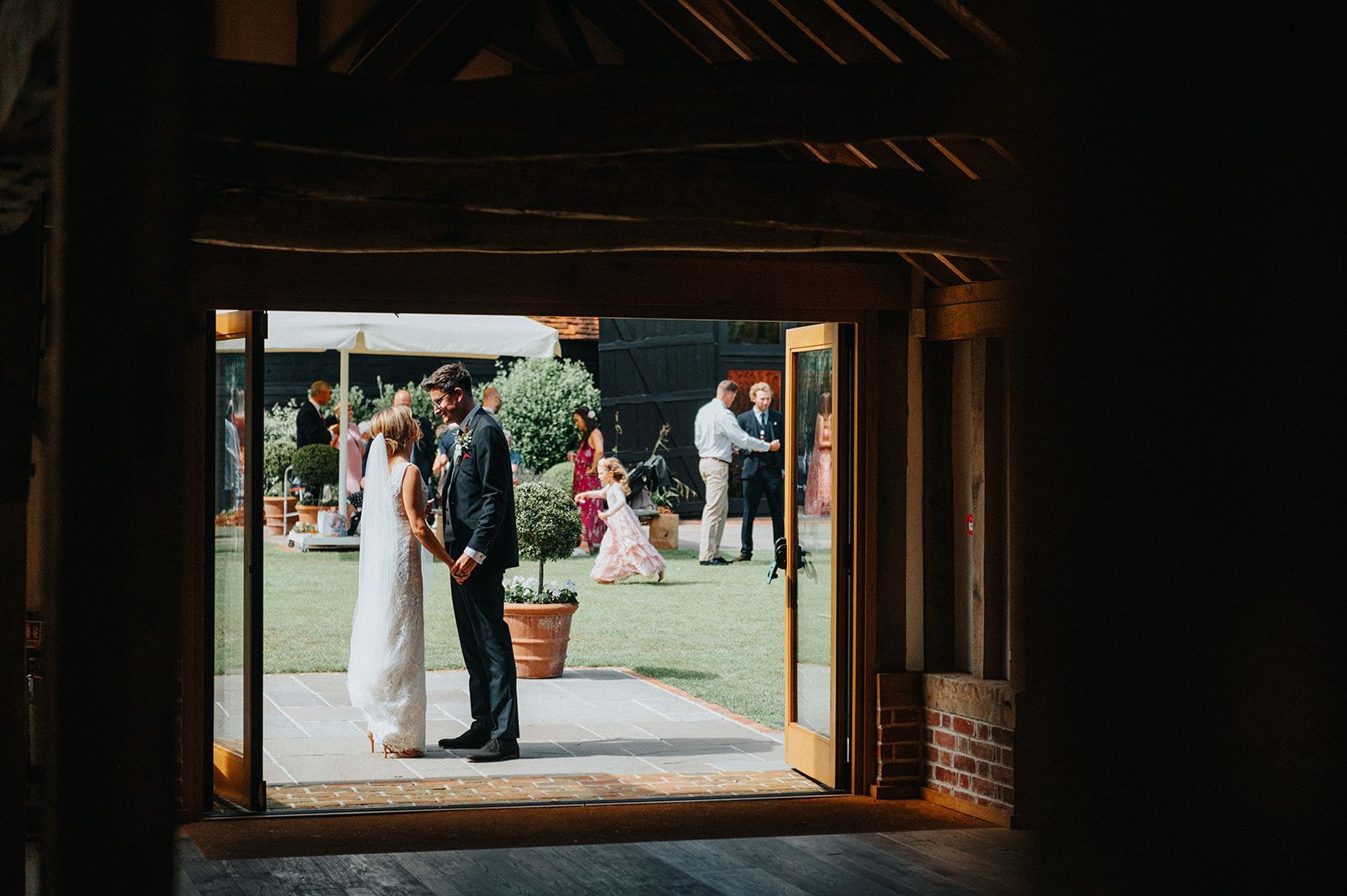 A bride and groom are standing in a barn holding hands.