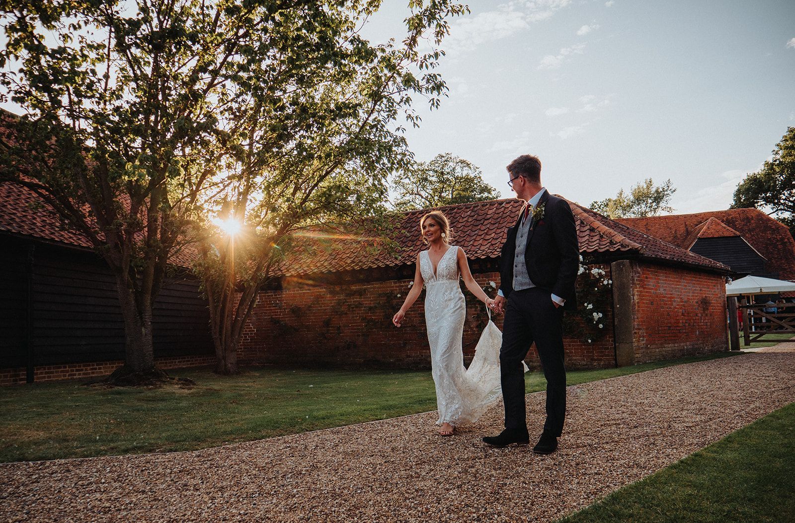A bride and groom are walking down a gravel road holding hands.