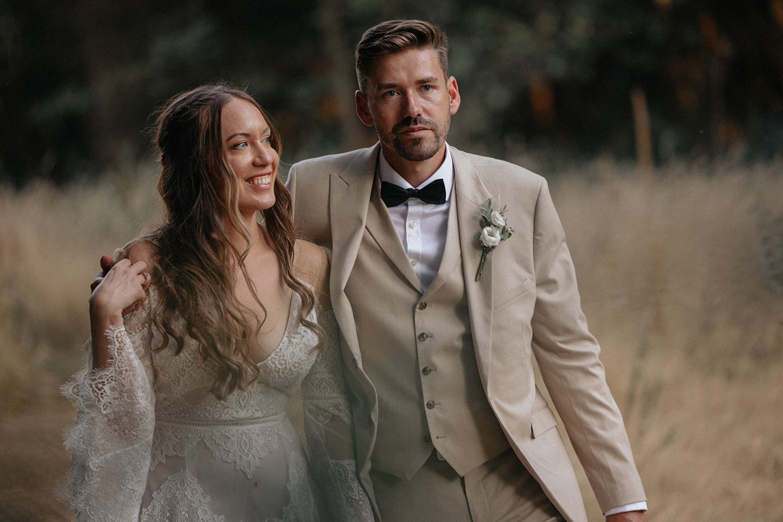 A bride and groom are standing next to each other in a field.